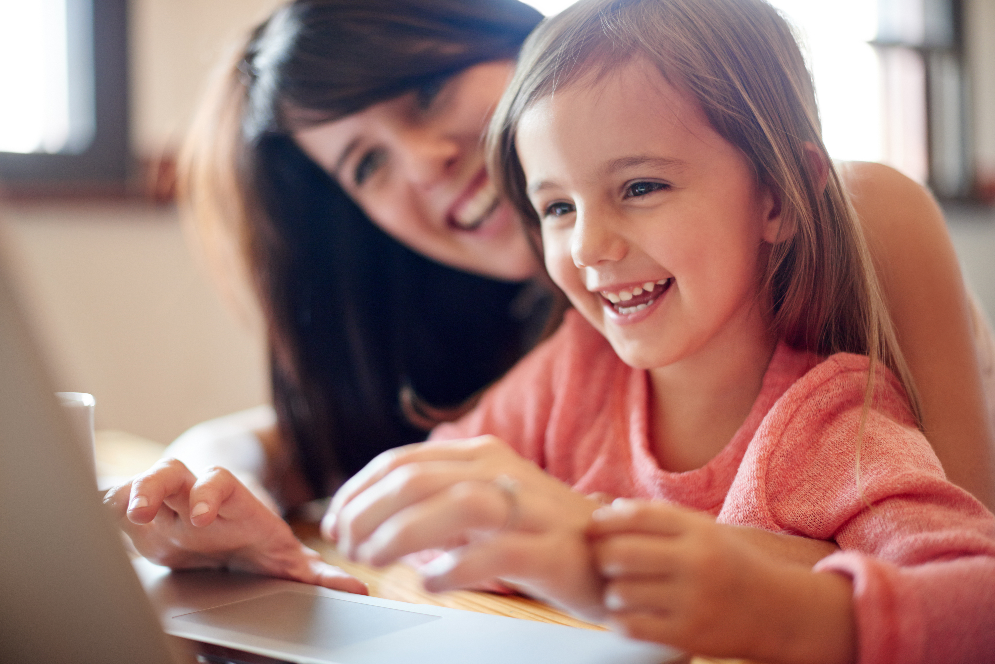 A mother and her daughter smiling while using a laptop together